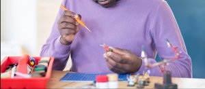 Teenage boy doing school work at home painting and building. He could use online therapy in New Jersey to help with his anxiety and other issues. Online counseling in New Jersey or telehealth can help!