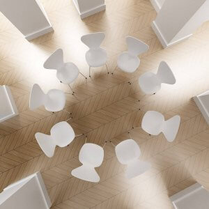 Overhead view of a modern room with geometrically arranged white tables and matching chairs on a herringbone-patterned wooden floor.