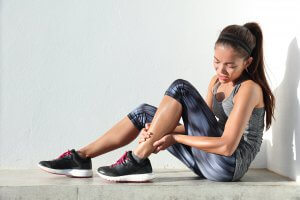 A young woman holds her leg while wincing in pain. This could represent a symptom of over-exercise that therapy for teens in Branchburg, NJ can offer support with overcoming. Learn more about Scotch Plains therapy and how online therapy in New Jersey can offer support. 
