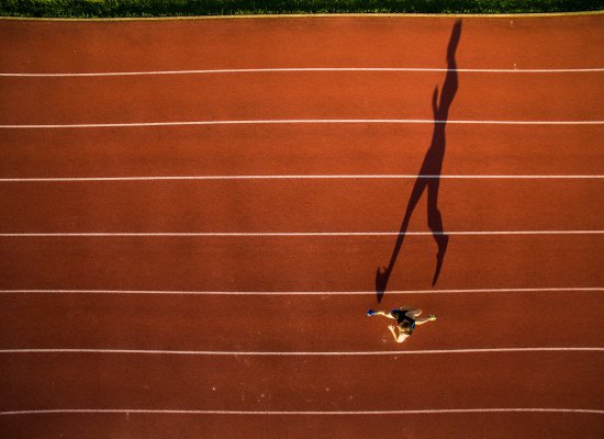 A top down view of a track runner and their long shadow. Learn how therapy for teens in Branchburg, NJ can offer support for young athletes by searching for online therapy in New Jersey or “therapist branchburg, nj”. They can offer support via online therapy for teens and more.