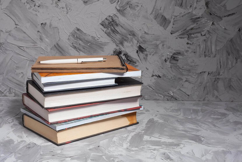 A stack of colorful books with a notebook and pen on top, set against a gray textured background. Learn more about overcoming back to school anxiety by searching for child counseling in Branchburg, NJ. Contact a child therapist in Branchburg, NJ to learn more about child counseling Scotch Plains, NJ and other services.