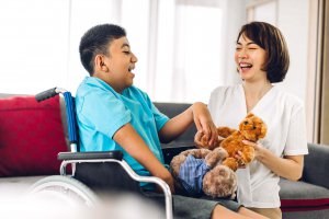 A mother smiles while playing with their child who is in a wheelchair. Learn how a child therapist in Branchburg, NJ can offer support by searching for child therapy in New Jersey. Child counseling in Branchburg, NJ can offer support today. 