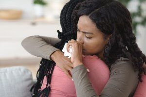 A sad black student hugs their friend while holding tissue paper for their tears. Learn more about therapy for teens in Branchburg, NJ and how an anxiety therapist in Branchburg, NJ can help address anxiety and other mental health concerns. 