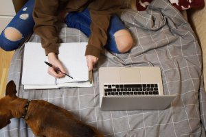 A top down view of a teen writing notes in their notebook while sitting on their bed with their dog. Learn how anxiety treatment in Branchburg, NJ can provide middle school anxiety help. Contact an anxiety therapist in Branchburg, NJ for more support in addressing child therapy for anxiety and more.