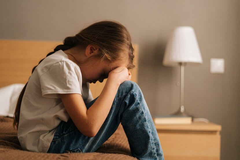 A child sits on a bed with her head resting on her knees. This could represent the isolation of anxiety that a child therapist in Branchburg, NJ can help address. Learn more about anxiety treatment in Branchburg, NJ or child therapy for anxiety. Search for an anxiety therapist in Branchburg, NJ today.