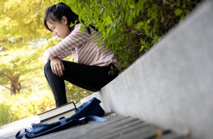 A child with an upset expression sits alone on a curb with a backpack and books nearby. This could represent academic issues in children that anxiety treatment in Branchburg, NJ can help improve. Learn more about child therapy for anxiety by contacting a child therapist in Branchburg, NJ today. 