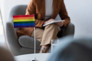 A close up of a rainbow pride flag on the desk of a person holding a clipboard and sitting across from another person. This could represent the support that an LGBTQIA+ therapist in Branchburg, NJ can offer. Search for LGBTQIA therapy Scotch Plains, NJ to learn more about lgbtq therapy in Scotch Plains, NJ today.