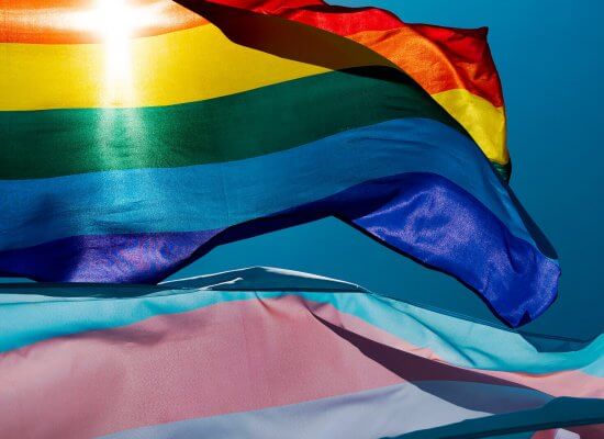 A close up of a rainbow pride flag next to a trans flag as they flutter in the wind against the light of the sun. Contact an LGBTQIA+ therapist in Branchburg, NJ to learn more about LGBTQIA therapy Scotch Plains, NJ and how LGBTQIA+ affirmative therapy in Somerville, NJ can help.