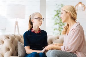 A parent and a teen sit on a sofa having an open conversation. The woman holds the girl's hand, both looking serious. Parenting Counseling in Scotch Plains NJ can help you understand your teen. 