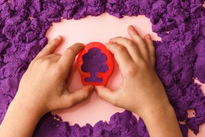 A close-up of a child's hands pressing a red plastic mold into purple kinetic sand. The child is shaping the sand, engaging in sensory play. Learn more about the power of play and how sandplay therapy in Branchburg, NJ can offer support. Search for child therapy in Somerville and contact a trauma therapist in Scotch Plains, NJ for more info.