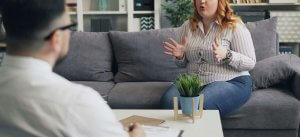 A woman with red hair and a striped shirt sits on a gray couch, gesturing with her hands while speaking to a therapist. This could symbolize the support an equestrian therapist in Branchburg, NJ can offer for adapting your identity. Learn more about EMDR therapy in Scotch Plains, NJ and how an EMDR therapist in Somerville, NJ can offer support. 