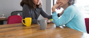 A younger woman in a gray sweater holds the hands of an older woman in a light blue sweater at a wooden table. They appear engaged in a serious and supportive conversation. Search for grief counseling in Westfield, NJ to learn more about how grief counseling NJ and an online therapist New Jersey can help today. 